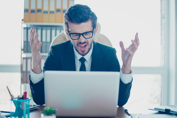 Angry young overworked businessman in formal clothing screaming at computer and gesturing with his hands