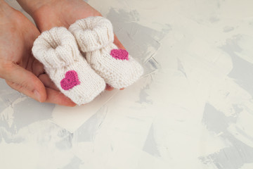 white knitted baby booties in mother hand, copy space. Waiting baby. Baby shower. New Born Girl