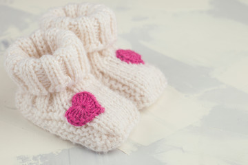 Obraz na płótnie Canvas white knitted baby booties with pink knitting heart, copy space, front view
