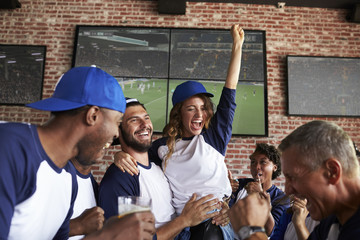 Friends Watching Game In Sports Bar On Screens Celebrating