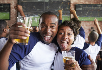 Portrait Of Couple Watching Game In Sports Bar On Screens