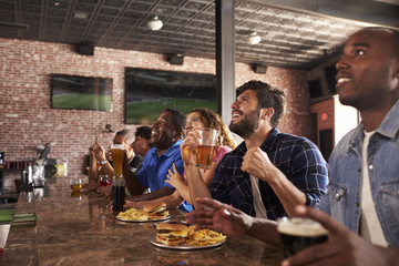 Friends At Counter In Sports Bar Watching Game