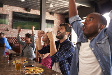 Friends At Counter In Sports Bar Watch Game And Celebrate