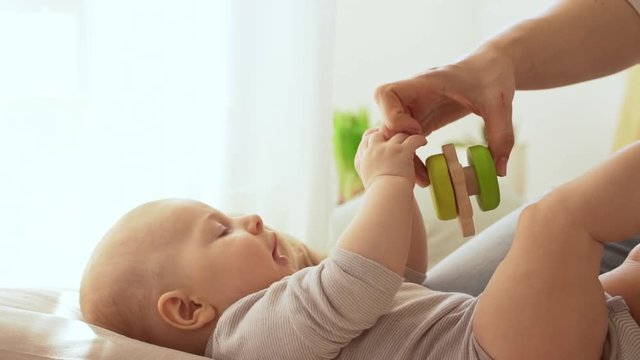Infant caucasian baby boy lying on back while his mother playing with rattle toy in slowmotion