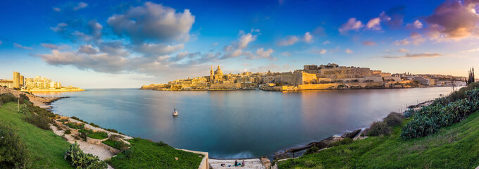Valletta, Malta - Panoramic skyline view of the ancient city of Valletta and Sliema at sunrise shot from Manoel island at spring time with sailing boat, blue sky, beautiful clouds and green grass