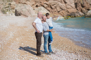 Family of grandfather father and son on a rocky beach on vacation enjoying time together