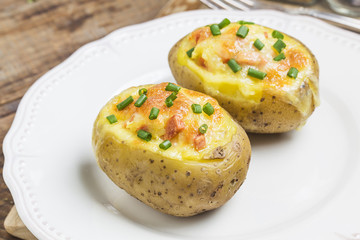 Close up of a hot baked potato topped with sour cream, bacon, green onions and cheddar cheese.