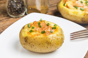 Close up of a hot baked potato topped with sour cream, bacon, green onions and cheddar cheese.