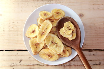 Dried banana Chips on a White plate with a wooden spoon