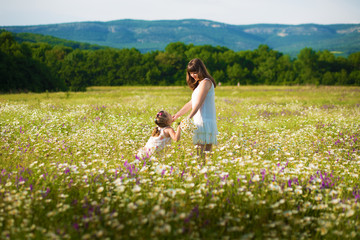Mom and daughter on a picnic in the chamomile field. Two beautiful blondes in chamomile field on a background of horse. Mother and daughter embracing in the chamomile field
