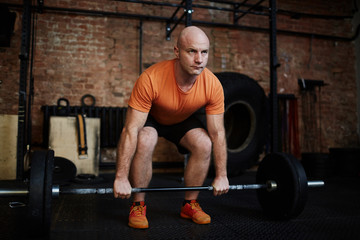 Fototapeta na wymiar Middle-aged athlete looking away with concentration while practicing deadlift technique in modern gym, full-length portrait