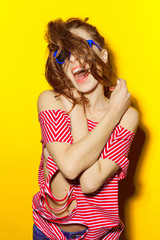 Beautiful young sexy girl in blue sunglasses and a red striped T-shirt laughing and having fun on a yellow background