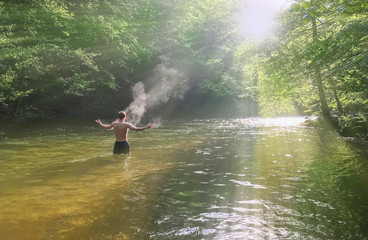 Man having a bath in Cerna  river with open arms, in front of the sun, in Herculane, Romania