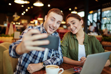 Leaving in memory warm evening with friend: pretty young woman and handsome bearded man taking selfie on smartphone while sitting in cozy coffeehouse