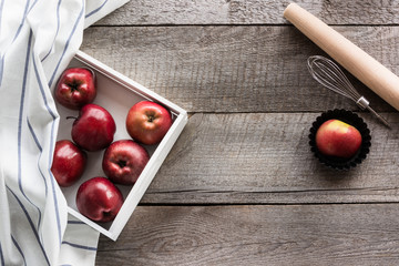 Ripe red apples in white birch tray on wooden board, kitchen utensils for baking and copy space for your text.