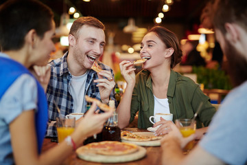 Group of cheerful friends eating delicious pizza and chatting animatedly while gathered in lovely...