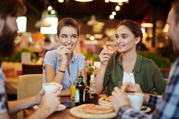Having double dating in pizza restaurant: two pretty young women and their bearded boyfriends gathered together and chatting animatedly, waist-up portrait