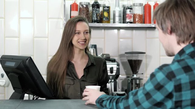 Man using mobile payment in a coffee shop, man take coffee and pay contactless with NFC chip, smiling woman near cahbox