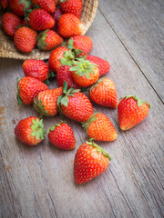 Fresh strawberries falling from bamboo basket on wooden background.