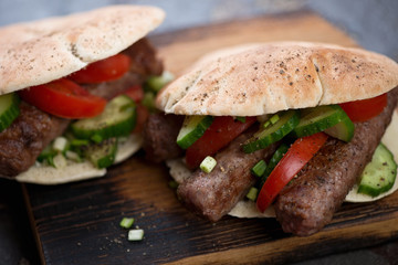 Closeup of grilled cevapcici sausages with fresh vegetables in pita bread, horizontal shot