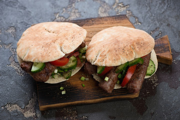 Pita bread with grilled cevapcici sausages and vegetables on a wooden serving board, studio shot