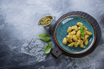 Potato gnocchi served with pesto sauce. Above view on a grey stone background with copy space, horizontal shot