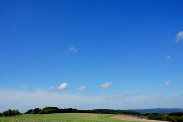 blauer Himmel mit wenigen Wolken über herbstlichen Feldern im Hunsrück
