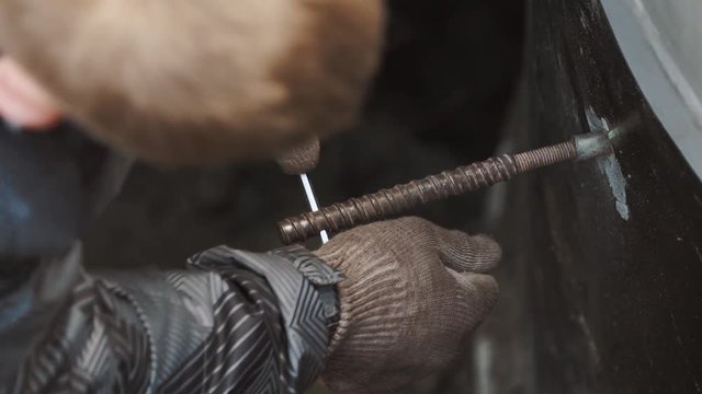 Close up men in work gloves and puffed jacket srew piece of metal rod from metal pipe in concrete