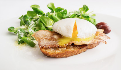 poached egg on fried toast with bacon, olives, and green salad sprinkled with parmesan