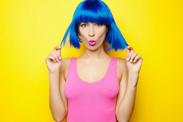 Beautiful young sexy girl in blue wig and pink swimsuit is having fun and fooling around on yellow background