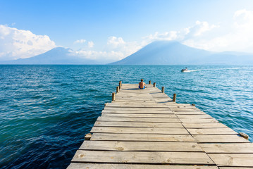Man sitting on Pier at San Marcos La Laguna with beaufiful scenery of Lake Atitlan and volcanos - Guatemala