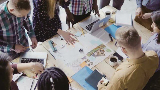 Top view of young team working on architectural project. Group of mixed race people standing near table and discussing.