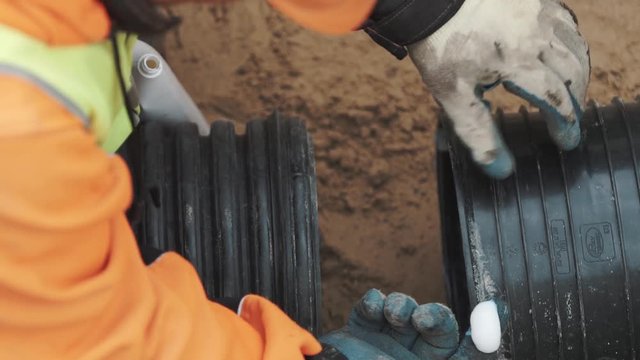 Worker squize white adhesive on finger in glove and apply it on edge of black plastic pipe. Slowmotion close up