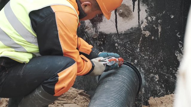 Worker applying sealant on stitch between black ribbed plastic pipe and concrete hole