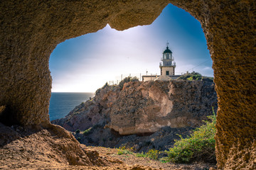 Lighthouse at Akrotiri through a frame of a window of a cave, Santorini, Greece.