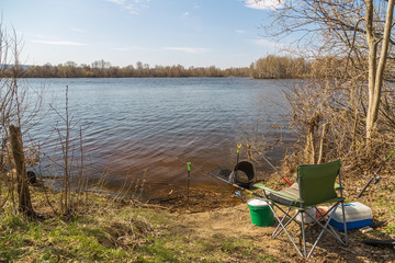 Obraz premium Place angler on the river Bank on a clear Sunny day in the spring. Fishing rods, fishing seat, tank, box of lures. The concept of active rest.