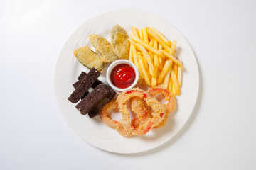 Fresh beer snacks assortment on a white plate. French fries, croutons and zucchini and sweet pepper
