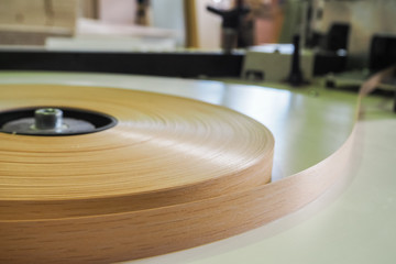 At a furniture factory edge plastic roll is fed into an edge banding machine.
