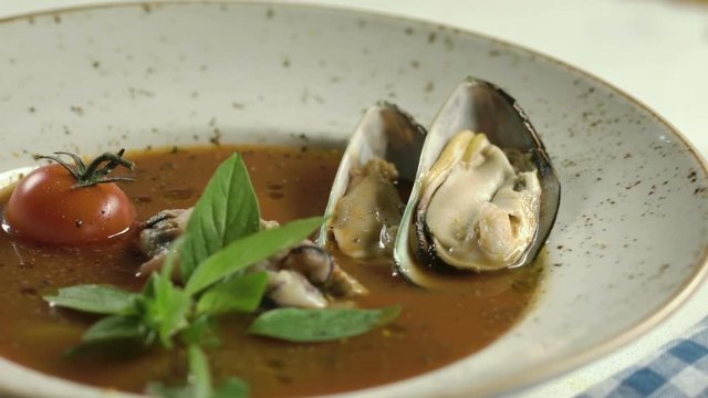 Tomato soup with seafood decorated with basil leaves and cherry tomatoes in white plate on the table. Hand adds the oyster. Slow motion.
