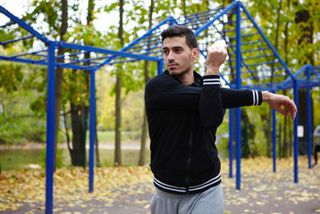 Obraz premium Beaded young man warming up in autumn park in order to prepare muscles for training, portrait shot