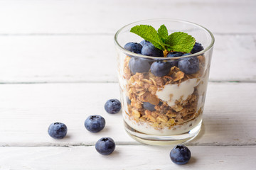 Granola with yogurt and blueberries in glass on white wooden table.
