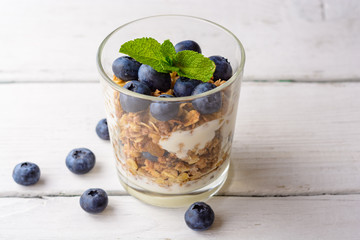 Fototapeta na wymiar Granola with yogurt and blueberries in glass on white wooden table.