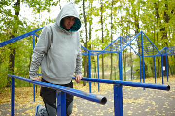 Naklejka premium Young sportsman in hoodie doing street workout exercise, legs bent at knee, full-length portrait