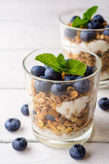 Granola with yogurt and blueberries in glass on white wooden table.