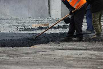 The worker is leveling the crumb of asphalt in the pit with a drag-roller before the paving with a road mini building roller.