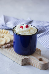 Rice pudding in a blue mug with berries and banana on a wooden board. Healthy breakfast. 