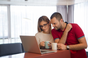 couple drinking coffee and using laptop at home