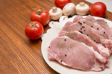 Slices of raw meat lie on a plate next to tomatoes and champignons