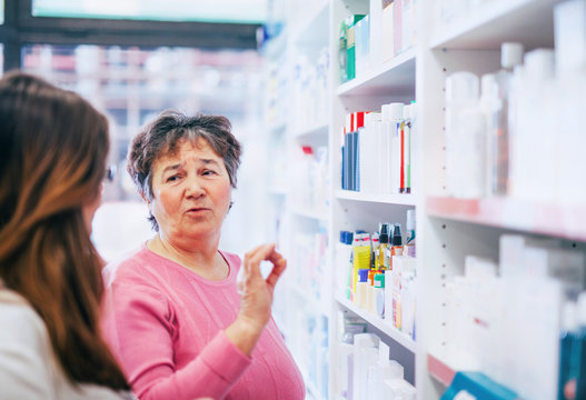 Pharmacist Discusses Medication Assortment With Senior Customer Beside Pharmacy Shelf