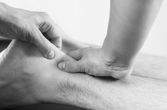 Closeup of hands of chiropractor/physiotherapist doing calf muscle massage to man patient  in white and black.